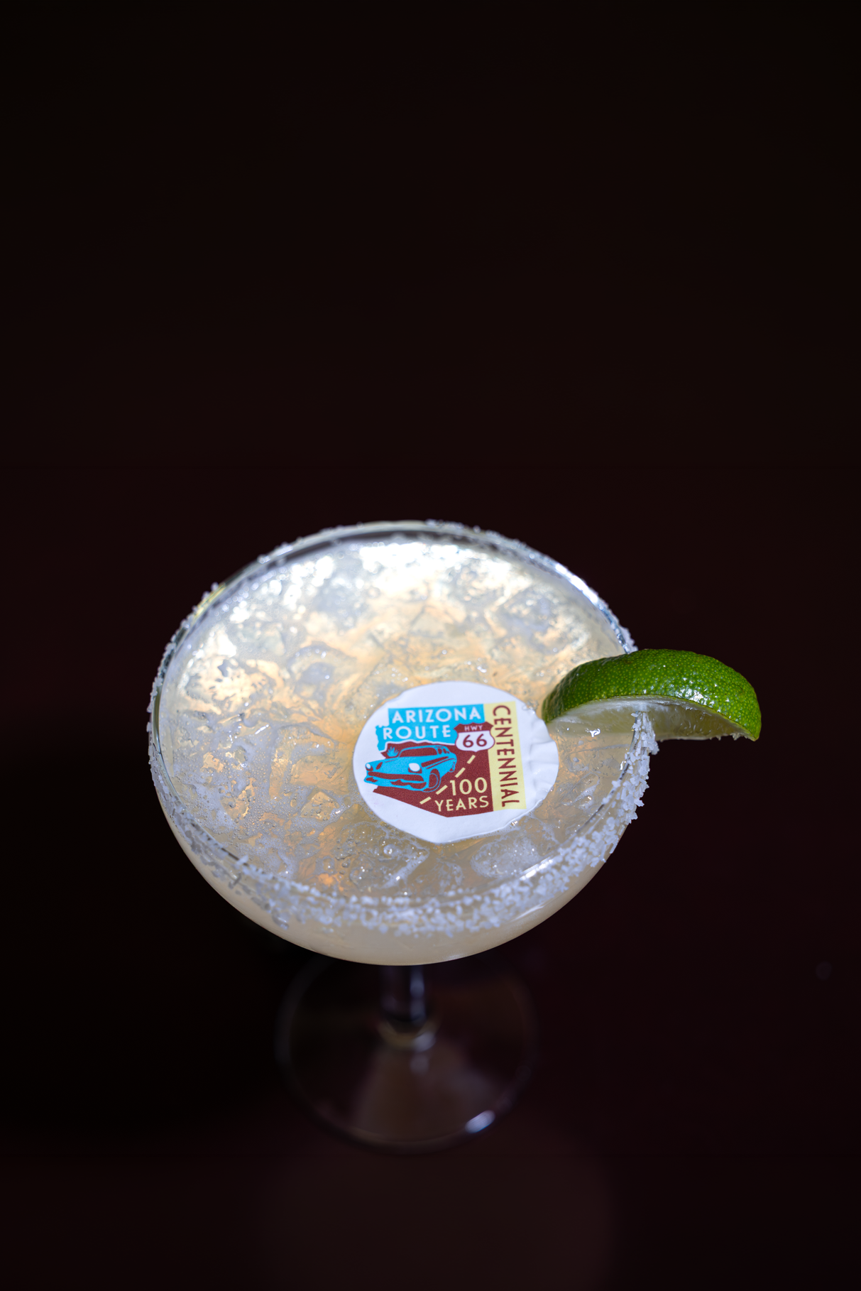 Icy margarita with a wedge of lime and a floating AZ route 66 Centennial badge floating in the drink
